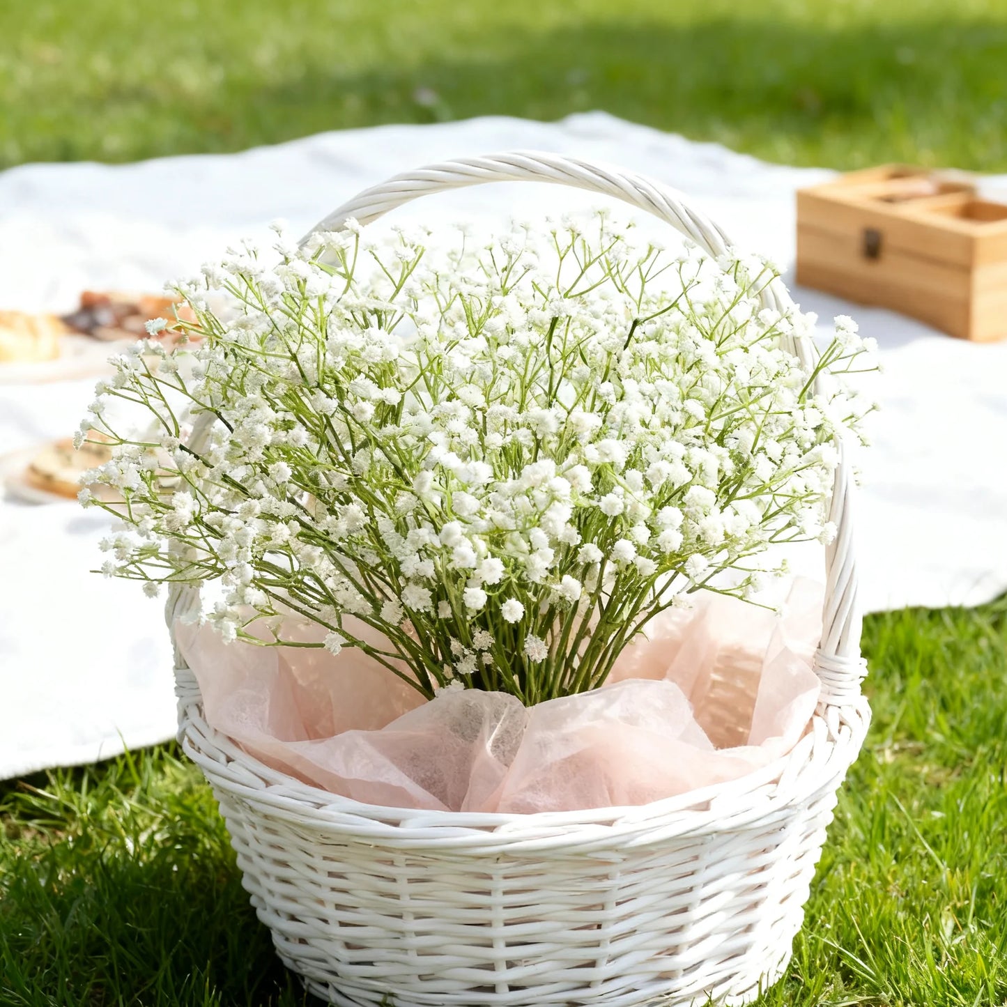 Main product photo — White baby’s breath wicker basket with light pink tissue on grass picnic blanket

Close-up flowers — Delicate baby’s breath blossoms with tiny white clusters and green stems

Top-down arrangement — Top view of handwoven white wicker basket filled with Gypsophila bouquet

Lifestyle picnic scene — Rustic picnic scene with floral basket, blanket, and wooden box outdoors

Bench scene with book and tea — Wicker flower basket on wooden bench beside open book and tea cup

Basket weave detail —